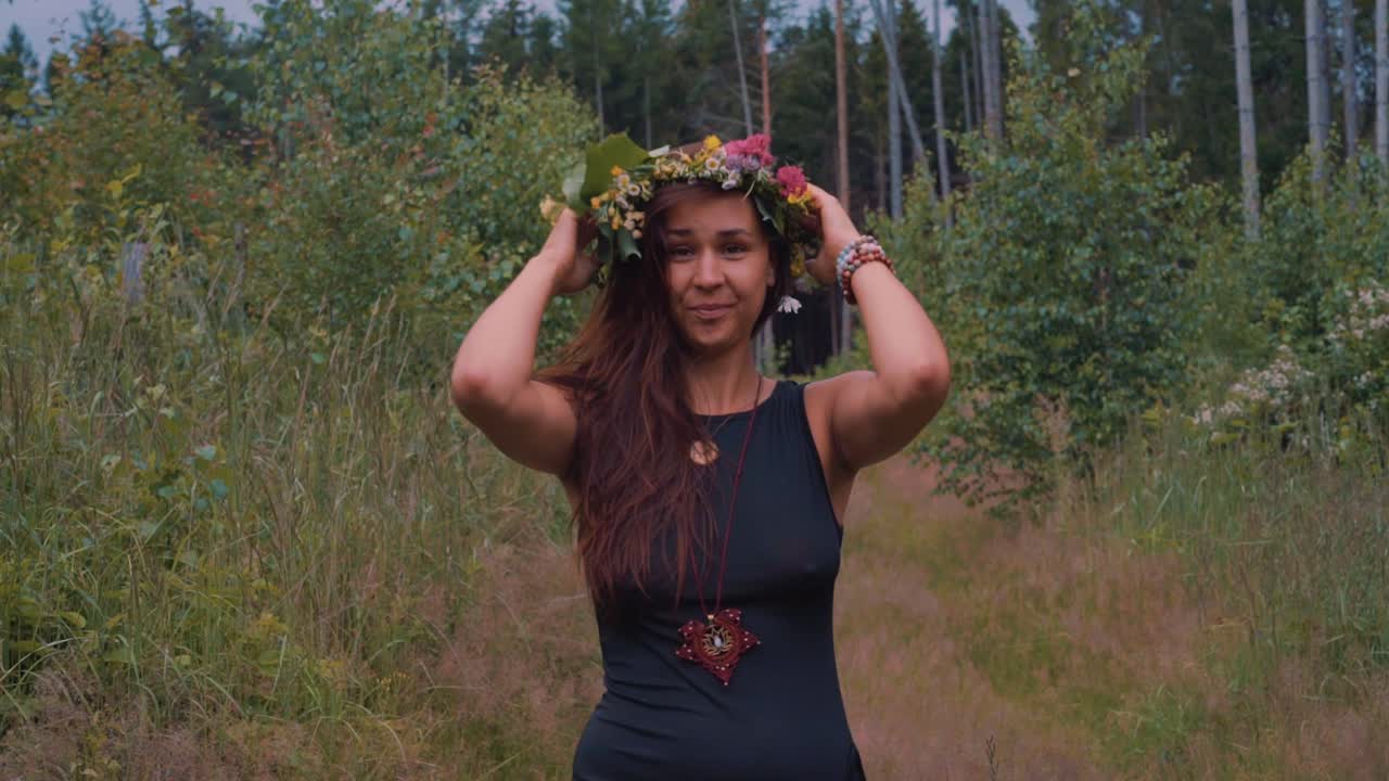 Girl with flower crown walks looking into camera in forest scenery,day