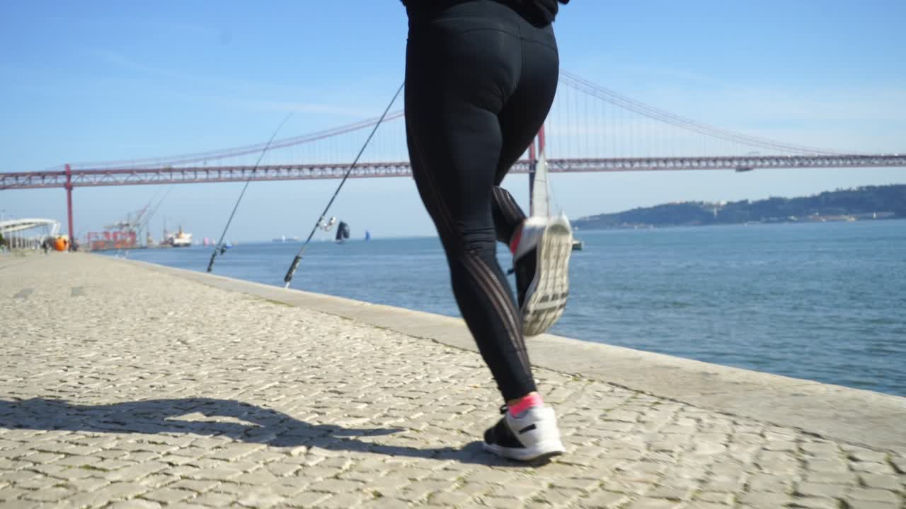 Low section of young sportswoman jogging along embankment