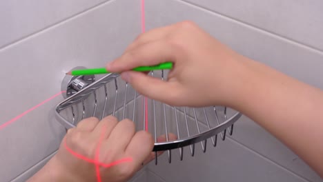 la regla láser mide líneas rectas desde el centro en la superficie de la baldosa. el artesano aplica un estante de esquina de metal y un soporte de círculos con lápiz en la pared para fijar los muebles en su lugar, vista superior.
