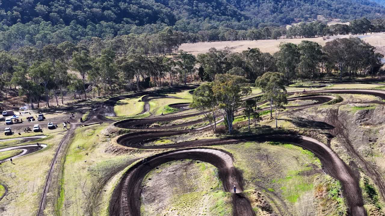 Drone slowly flies over winding motocross dirt track, sunny day, rural landscape, wide shot