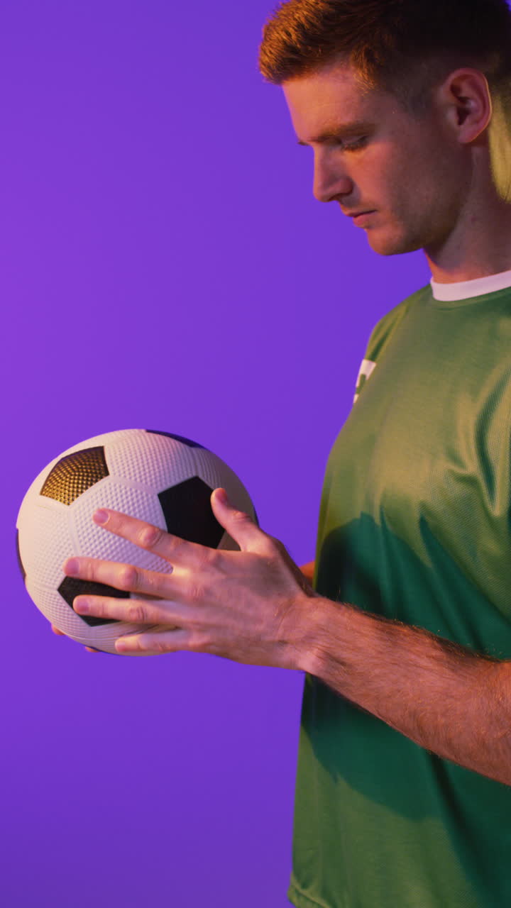 Video verticale di un calciatore maschio caucasico con un pallone da calcio su illuminazione rosa neon.
