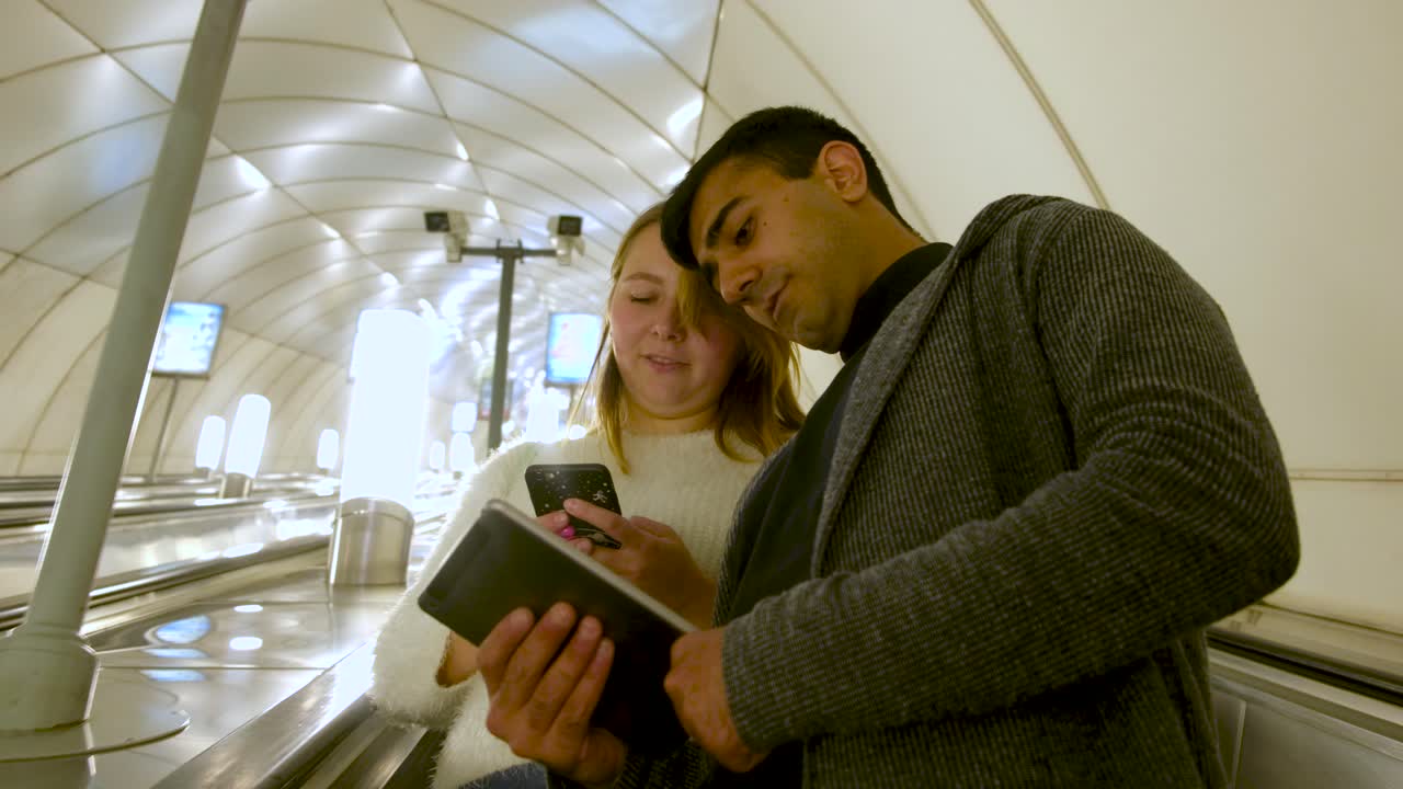 pareja usando dispositivos en una escalera mecánica del metro