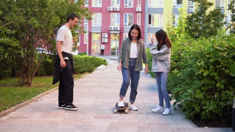 happy japanese girl trying to skateboard while her two friends helping her