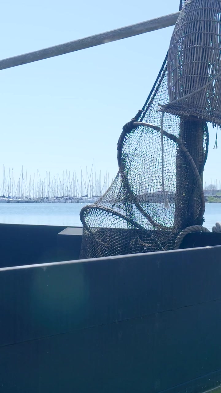 Reti e trappole da pesca tradizionali su una barca di legno in un porto turistico.