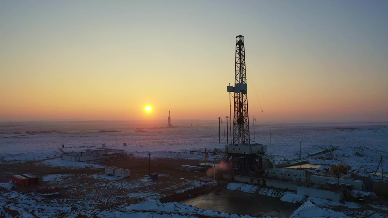 Close aerial view of drilling rig at sunrise in snowy oilfield.