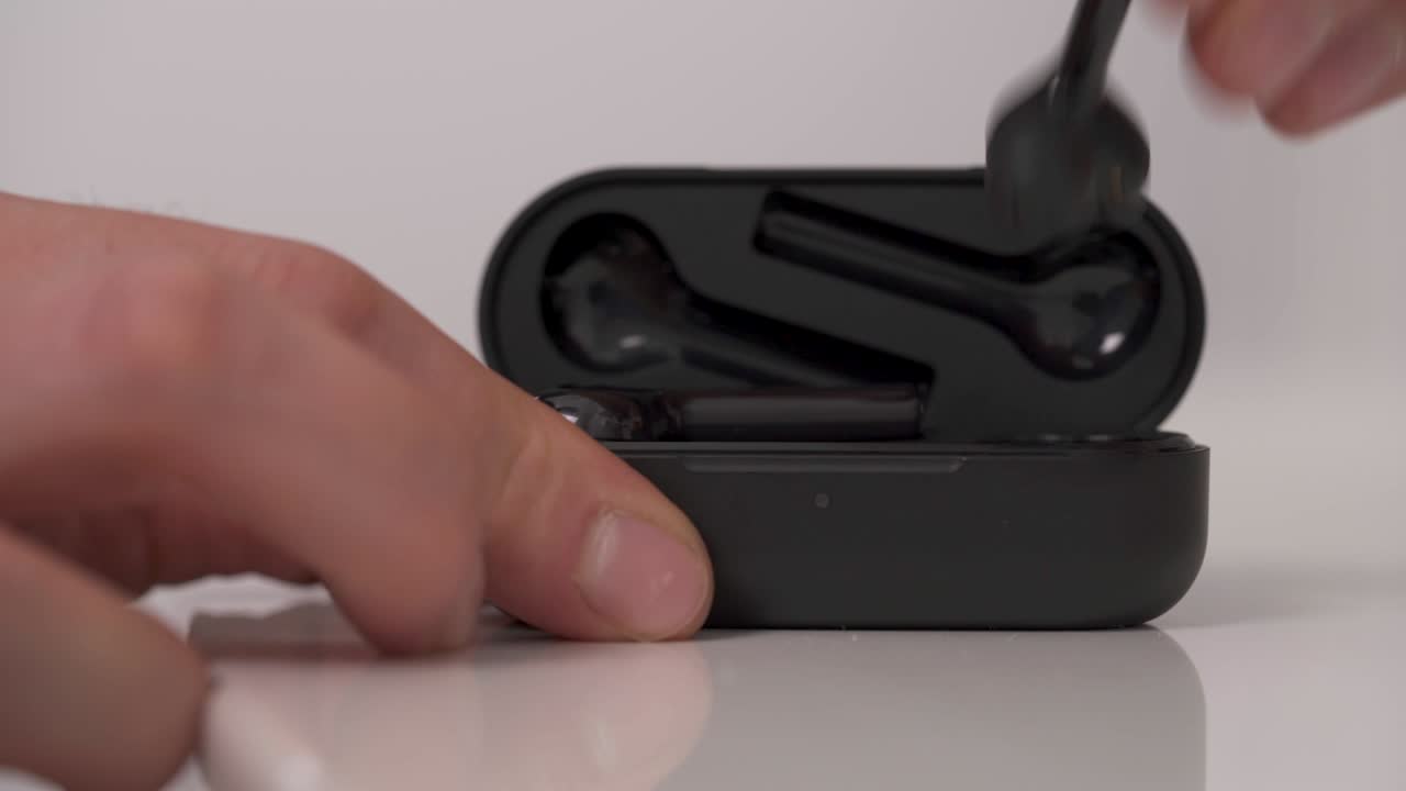 auriculares inalámbricos negros aislados sobre un fondo blanco. mano masculina sacando el auricular inalámbrico de la caja de carga