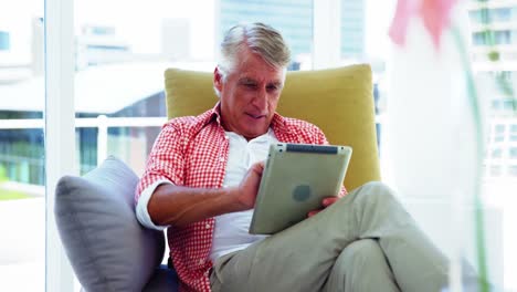 Mature-man-sitting-on-sofa-and-using-digital-tablet-in-living-room