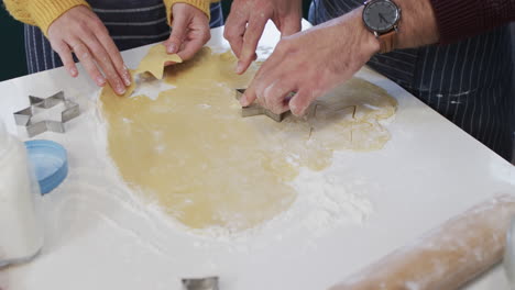 Midsection-of-diverse-couple-baking-christmas-cookies-in-kitchen-at-home,-in-slow-motion