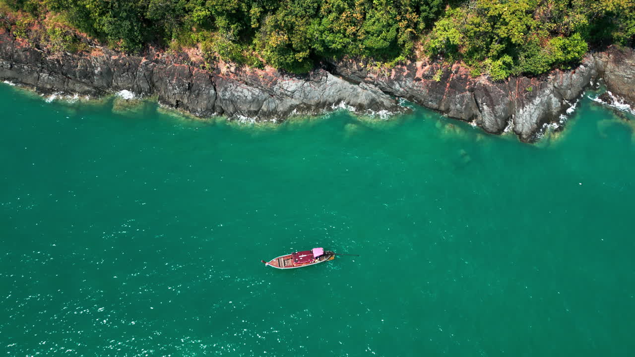 Aerial View of a Longtail Boat on Turquoise Water with a Rocky Coastline and Lush Vegetation