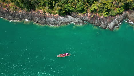 aerial view of a longtail boat on turquoise water with a rocky coastline and lush vegetation