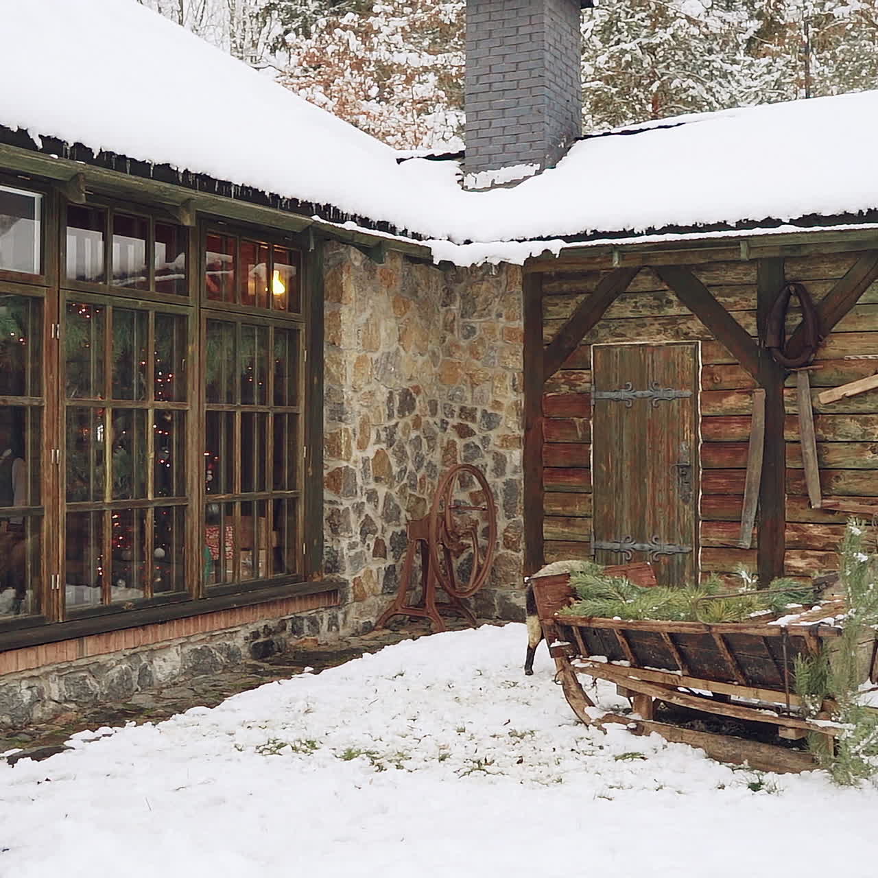 Beautiful cottage on the snowy background outdoors. Wooden sledge and a nice sheep standing in the street near the cozy building in the forest in winter.