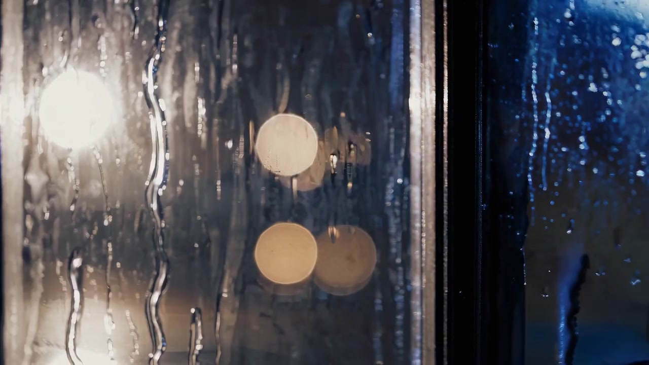 Raindrops Falling on a Window Pane with Blurred City Lights at Night