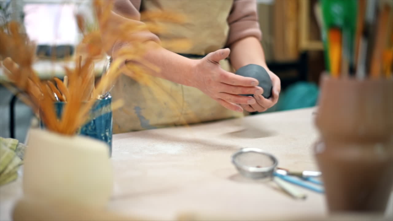 The master of sculpting pottery working in a studio. Kneading a piece of clay with her hands. Tools on the table. Slow motion