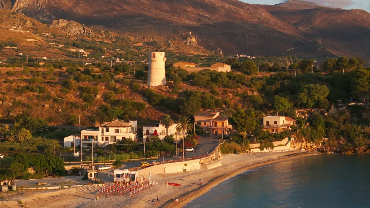 Push-in tilt-up aerial drone of Guidaloca Beach, white architecture, and Sicilian nature, Sicily, Italy during sunrise showing vast landscape and serene scenery