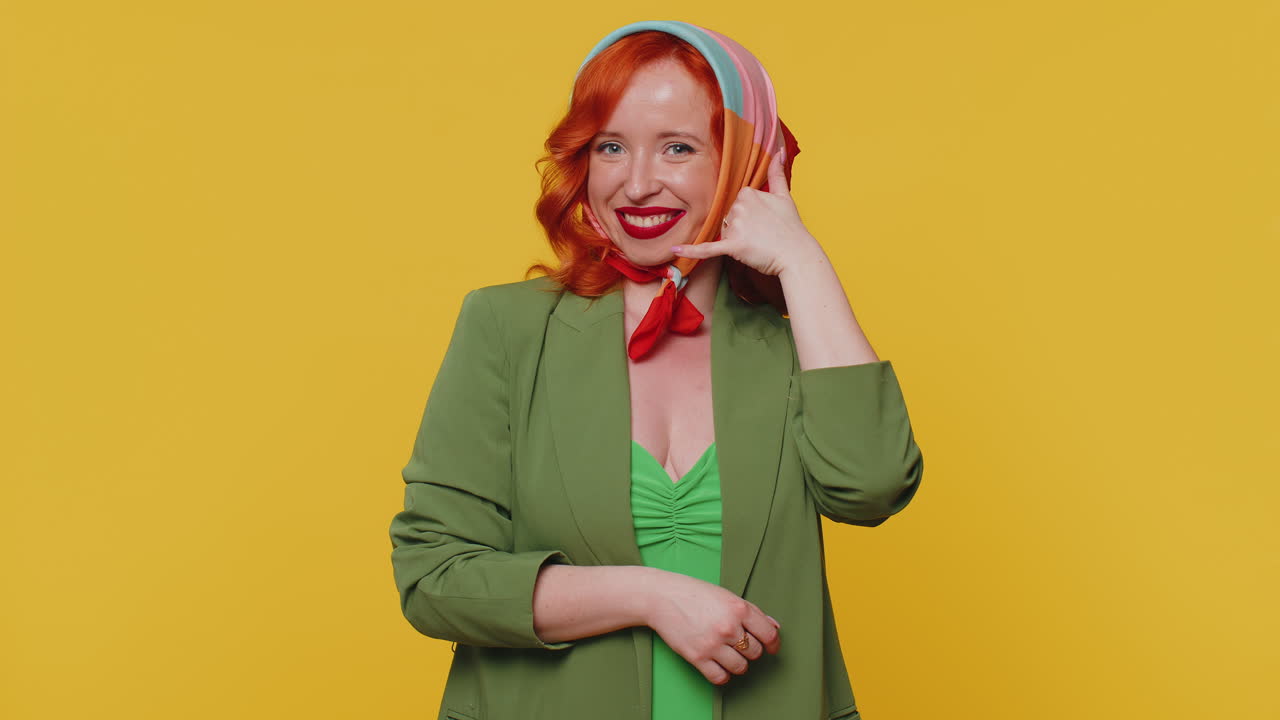 은 머리카락의 젊은 여성 판매자는 카메라를 보고 전화 제스처를 하고 있습니다.