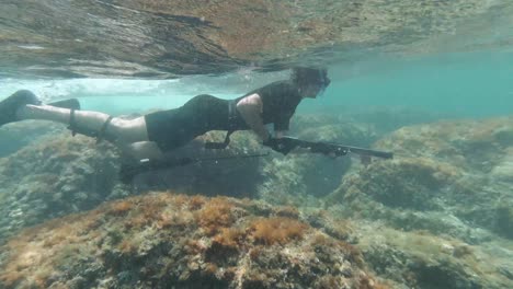 spearfisher snorkeling in very shallow water, rocky sea floor and strong current looking for fish in mediterranean sea