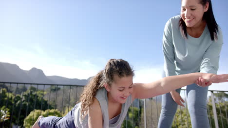 happy biracial mother and daughter practising yoga on terrace in sunny day, slow motion, copy space