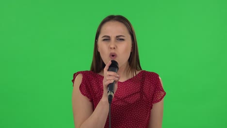 retrato de una niña tierna en vestido rojo está cantando en un micrófono y moviéndose al ritmo de la música. pantalla verde