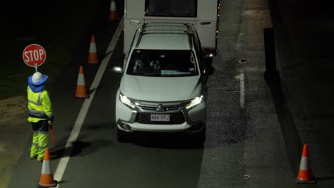 traffic guard in reflective uniform giving a go signal on cars travelling at night - traffic at the nsw - qld state border checkpoint - gold coast, australia. - high angle shot