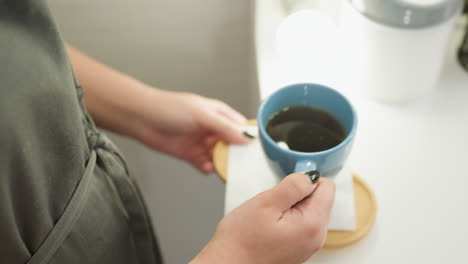 beautician carefully holds blue tea cup on tray lined with white tissue, showcasing well-manicured black nails while gently placing it on table in clean salon, reflecting calm, attentive hospitality