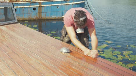 driven young man sands boat cabin roof planks by hand in sunshine