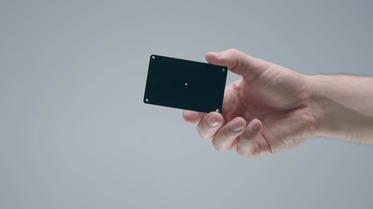 mano masculina mostrando una tarjeta bancaria de plástico negra con puntos de seguimiento en el fondo gris del estudio, video publicitario