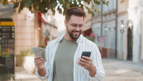 hombre caucásico feliz contando dinero en efectivo usando una aplicación de calculadora de teléfono inteligente en la calle de la ciudad