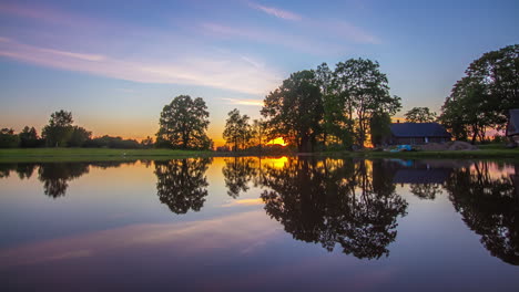 Zeitrafferaufnahme-Des-Sonnenuntergangs-Im-Hintergrund-Mit-Blick-Auf-Einen-See-Neben-Einem-Holzhaus-Während-Der-Abendzeit