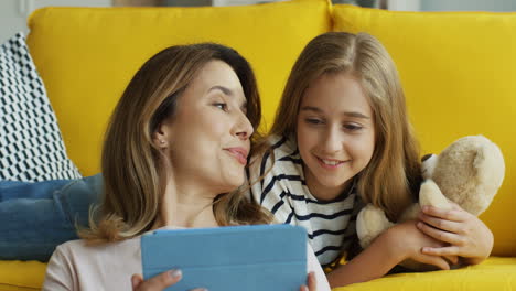 close up view of blonde mother with her teen daughter watching something on a tablet and smiling