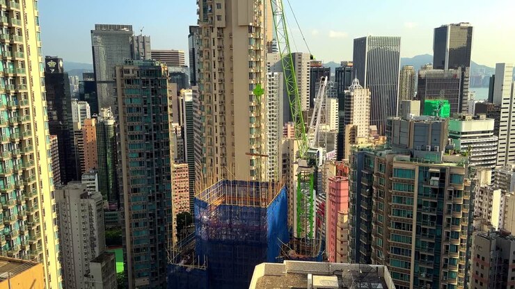Tower Crane Hoisting Wooden Planks onto Skyscraper Construction Site Surrounded by Residential Buildings in Hong Kong's Concrete Jungle