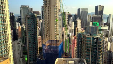 tower crane hoisting wooden planks onto skyscraper construction site surrounded by residential buildings in hong kong's concrete jungle