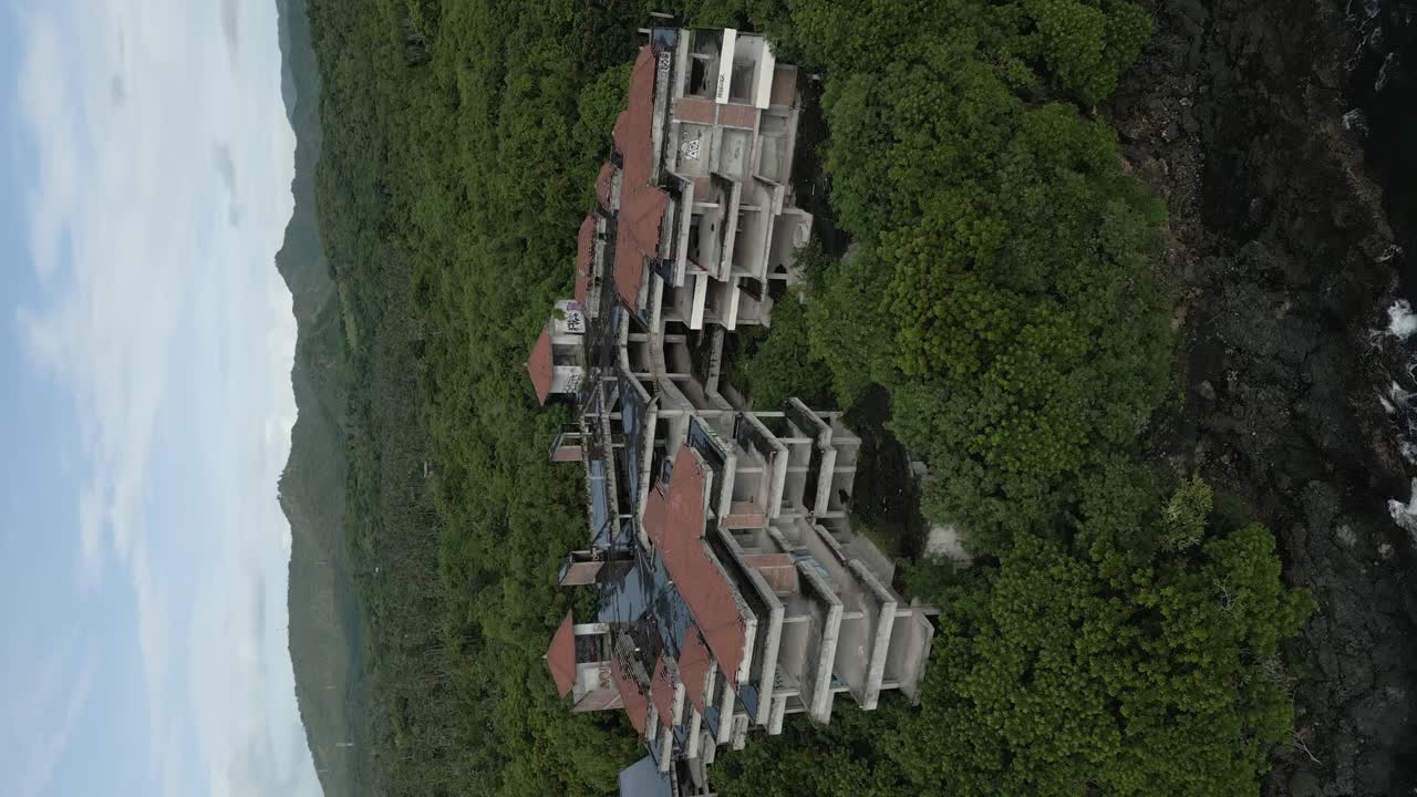 인도네시아의 녹색 자연 속에서 버려진 호텔의 수직 공중 드론 패닝 샷