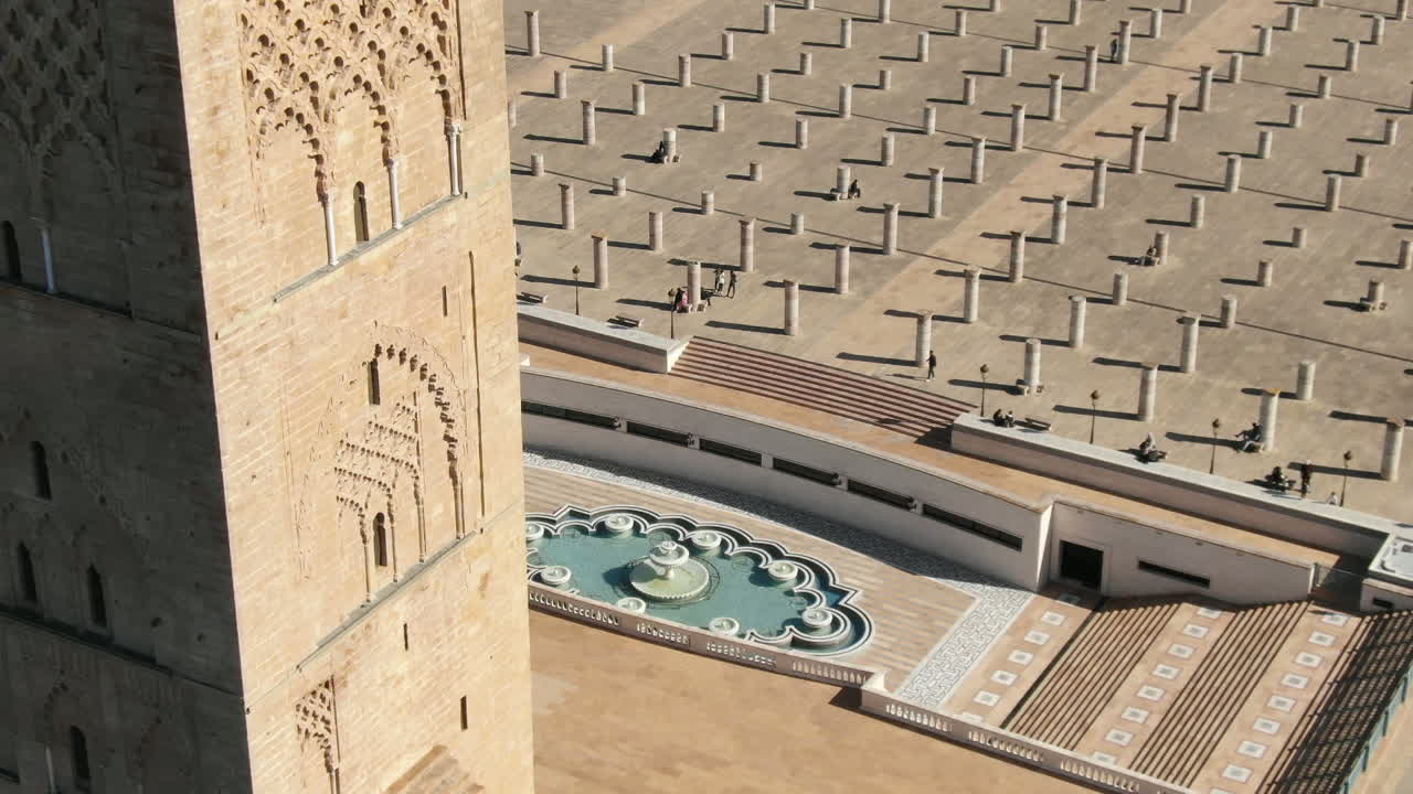 Ripresa HD dettagliata che mostra le intricate sculture in pietra in stile almohade della Torre di Hassan a Rabat. L'inquadratura cattura una bellissima fontana geometrica e la vasta piazza di antiche colonne sullo sfondo