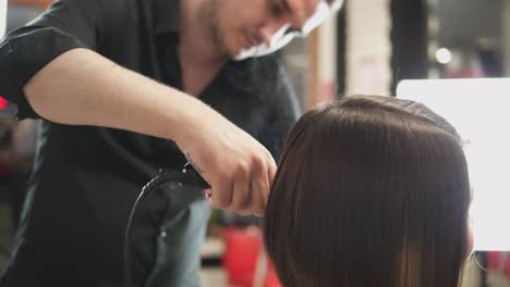 Professional-hairdresser,-stylist-makes-professional-hairstyle-of-young-woman-in-beauty-studio,-using-barrette-for-fixing-hairdo.-Hair-straightening-Beauty-and-haircare-concept