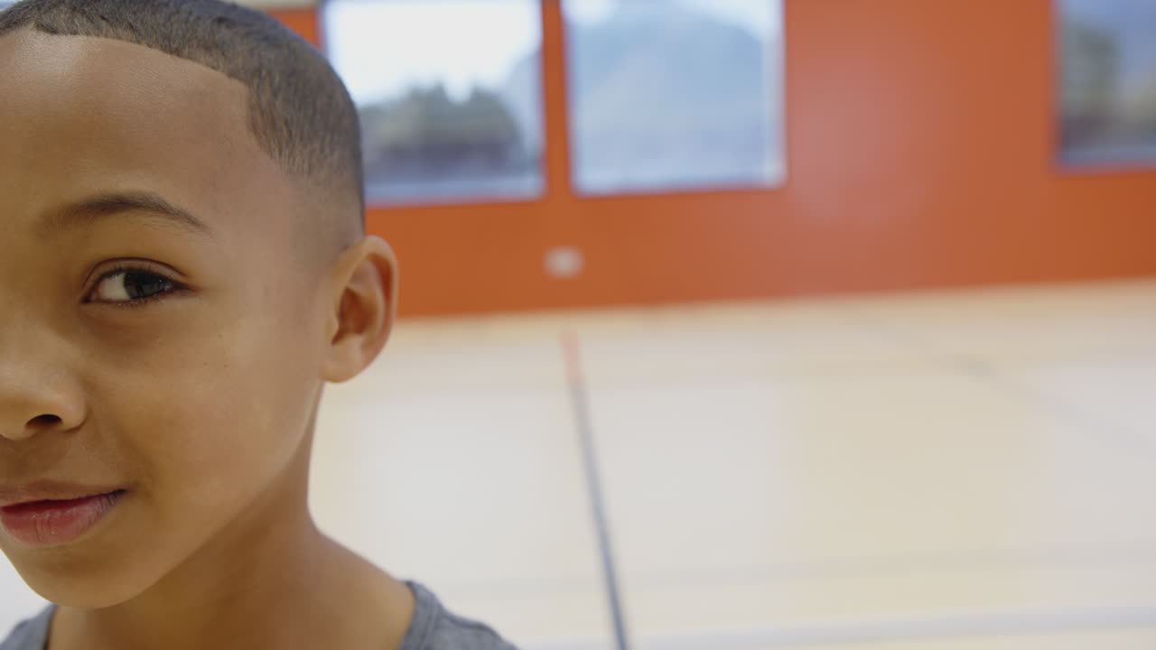 Nella palestra della scuola, un ragazzo sorridente che guarda la telecamera, divertendosi.