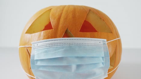 Komposition-Aus-Orangefarbenem-Halloween-Kürbis-Mit-Gesichtsmaske-Vor-Weißem-Hintergrund