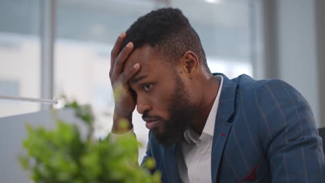 close up of stressed and upset african man with laptop working at office