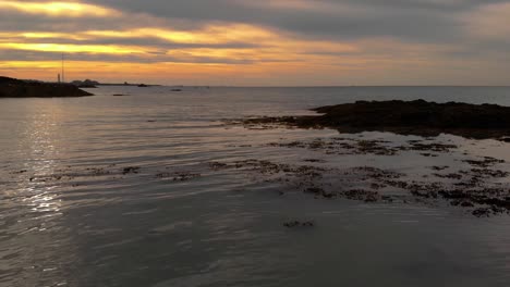 Aerial-Drone-shot-slowly-pushing-out-over-the-sea-into-St-Aubin's-Bay-at-sunset-in-Jersey,-Channel-Islands