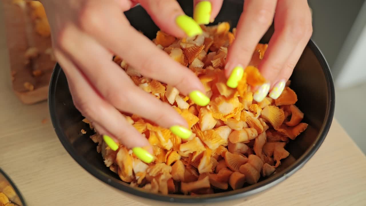 Female hands slowly drop chopped chanterelles into black bowl in rustic kitchen