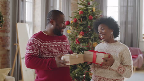 joyous african american couple holding xmas gifts and speaking at home