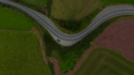 Aerial-birds-eye-overhead-top-down-ascending-view-of-car-standing-aside-road-winding-between-fields-and-meadows-in-countryside.-Ireland