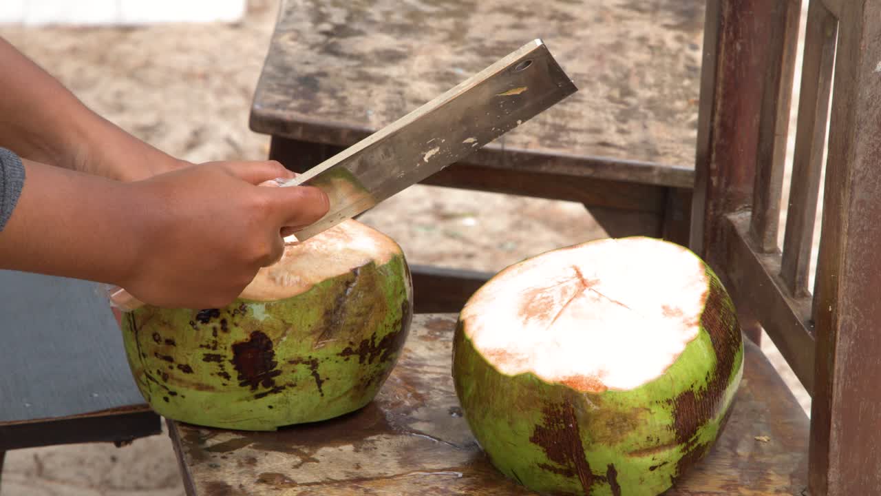 Close-up shot of hands skillfully chopping a green coconut with a cleaver outdoors