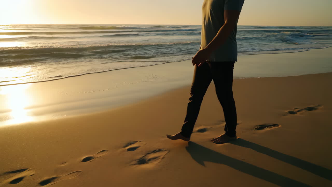 Person walking on a sandy beach at sunset, leaving footprints