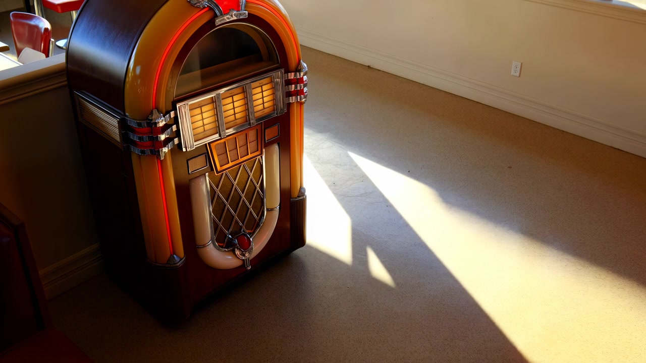 Un jukebox è splendidamente illuminato dalla luce del sole in un ambiente interno vintage con pavimento e parete in legno, catturato da una vista laterale leggermente elevata, evocando un'atmosfera luminosa e nostalgica.