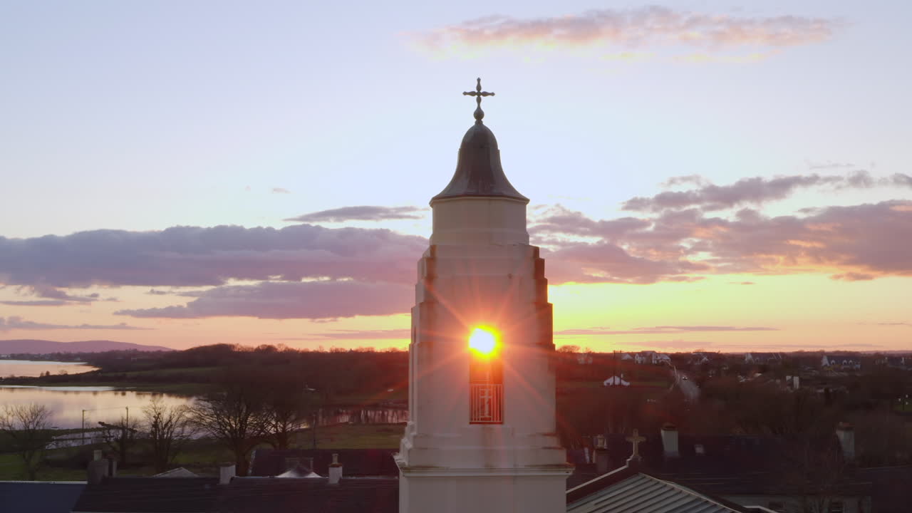 Sun flare appears between Clarinbridge church steeple against rich sunset sky in warm dusk glow