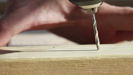 man drilling hole through lumber in sunlight, close, pan left, slow motion