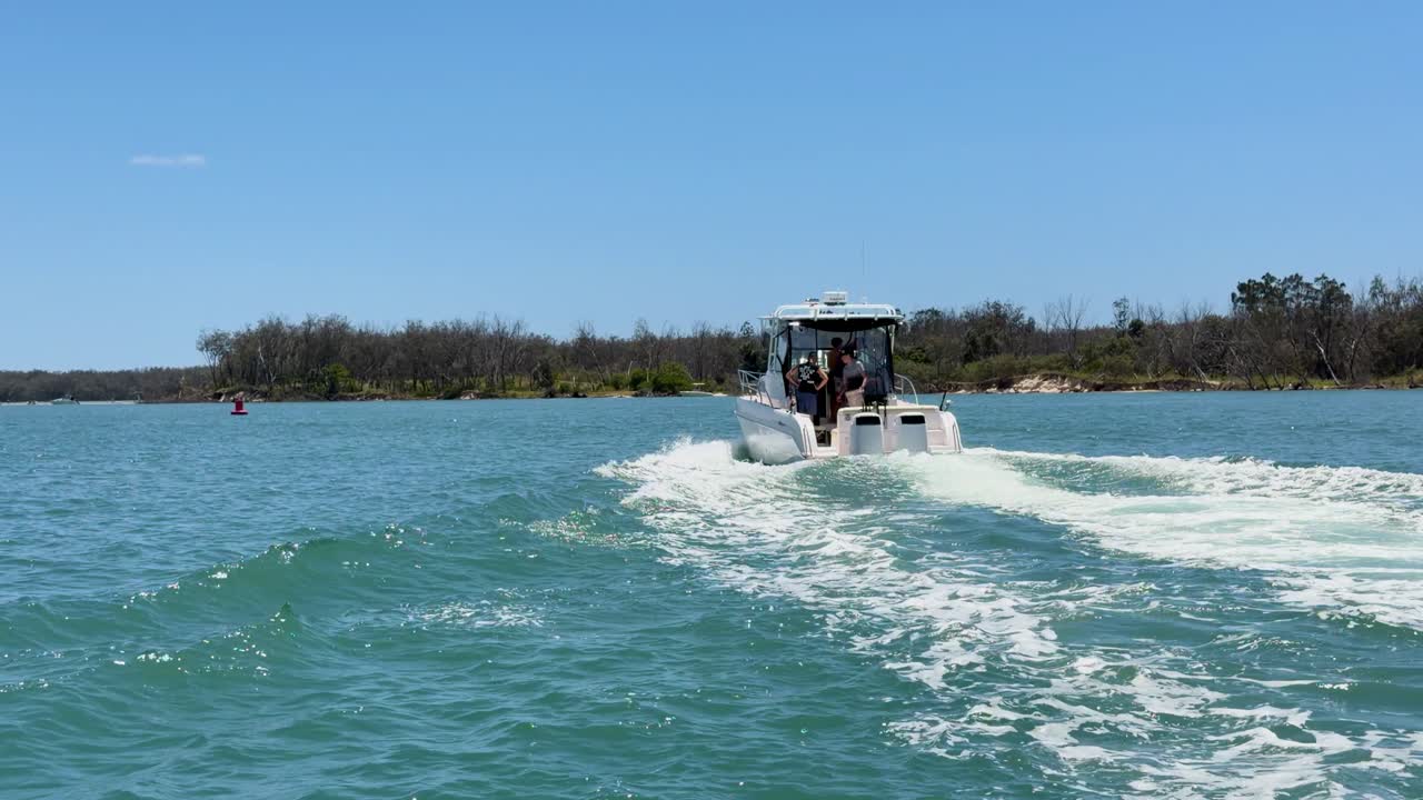 A white motorboat cruises across calm blue water leaving a prominent wake under clear skies