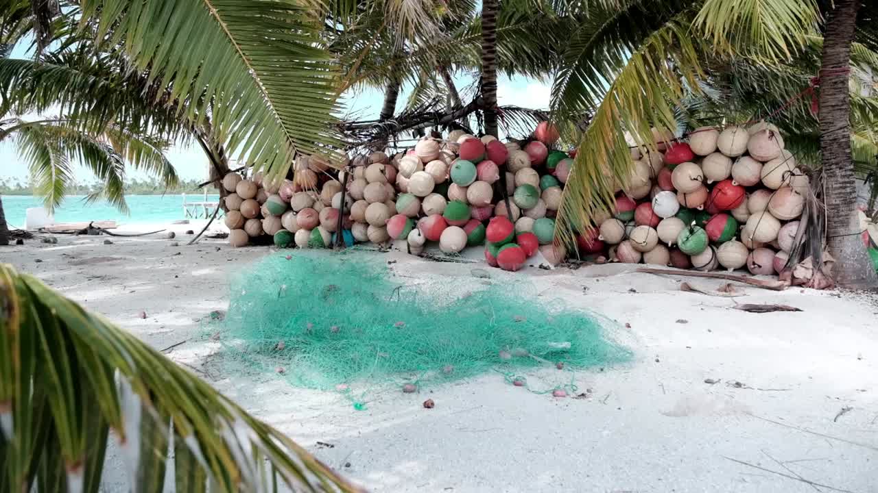 una enorme pila de boyas de pesca de plástico coloridas y redes bajo algunas palmeras en una isla tropical