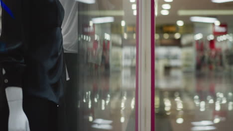 close-up of clothing rack and mannequins inside retail store with blurred mall background, showcasing elegant garment arrangements, subtle lighting, and reflective glass panels