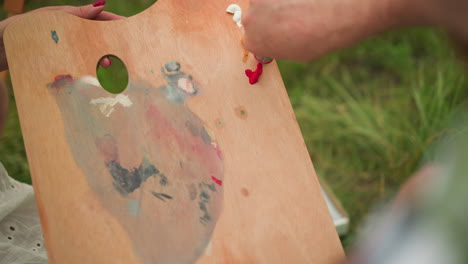 a close-up shot of a collaborative moment in art creation, with a woman's hand holding a wooden palette as a man's hand carefully squeezes out red paint onto it